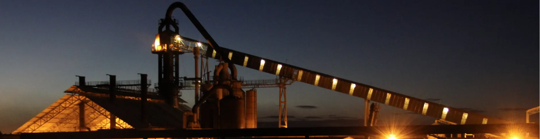 Na imagem vemos um dos altos fornos de nossa usina siderúrgica de aço.

O processo de altos-fornos em uma siderúrgica é a etapa fundamental para a produção de ferro-gusa, matéria-prima essencial para a fabricação do aço. Ele consiste em um forno vertical de grandes dimensões, onde ocorre a transformação do minério de ferro em ferro líquido por meio de um processo de redução química e fusão.

O Minério de Ferro é utilizado como fonte de ferro. O nosso Carvão vegetal é utilizado como combustível e agente redutor. Fundentes (como calcário) são utilizados para remover impurezas formando escória.

Nesse processo, o carvão reage com o ar quente injetado pela parte inferior, gerando calor intenso e monóxido de carbono (CO), que reduz o minério de ferro a ferro metálico. A temperatura no interior pode ultrapassar 2.000 °C, permitindo a fusão do ferro. O ferro líquido (gusa) é coletado na parte inferior do alto-forno. A escória, formada pelas impurezas fundidas, é removida separadamente.

Com isso, o ferro Gusa é usado diretamente em processos de produção do nosso aço.