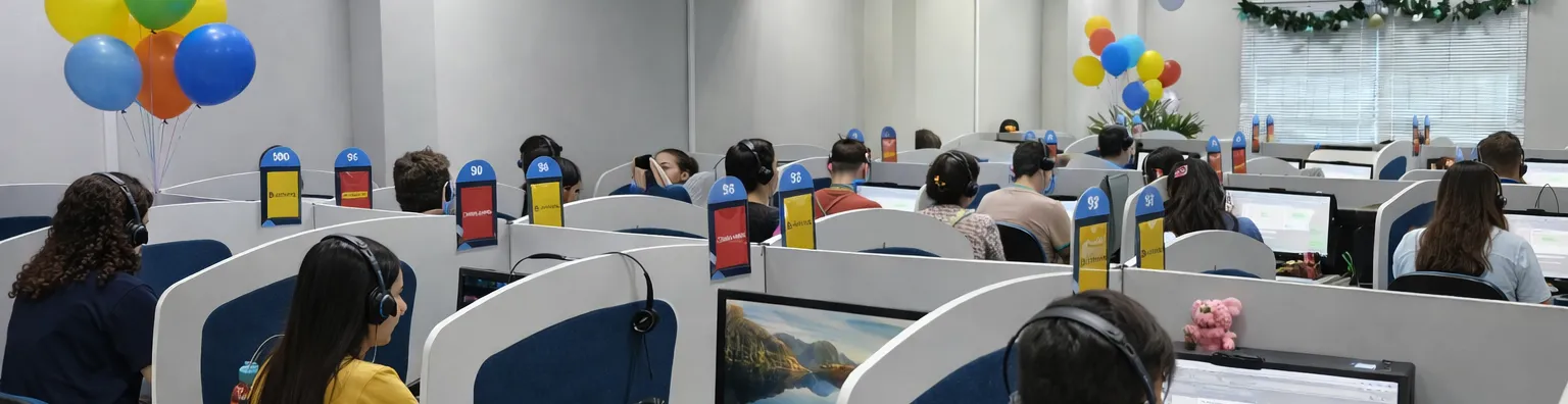 Ambiente de call center: escritório amplo e iluminado, com várias pessoas trabalhando em mesas organizadas, usando computadores e headsets. O clima é profissional e colaborativo, com luz natural e cores claras que transmitem um ambiente agradável e acolhedor.