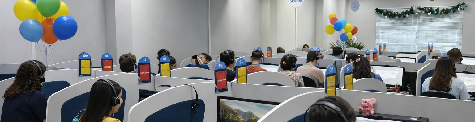 Ambiente de Call center: escritório amplo e iluminado, com várias pessoas trabalhando em mesas organizadas, usando computadores e headsets. O clima é profissional e colaborativo, com luz natural e cores claras que transmitem um ambiente agradável e acolhedor.