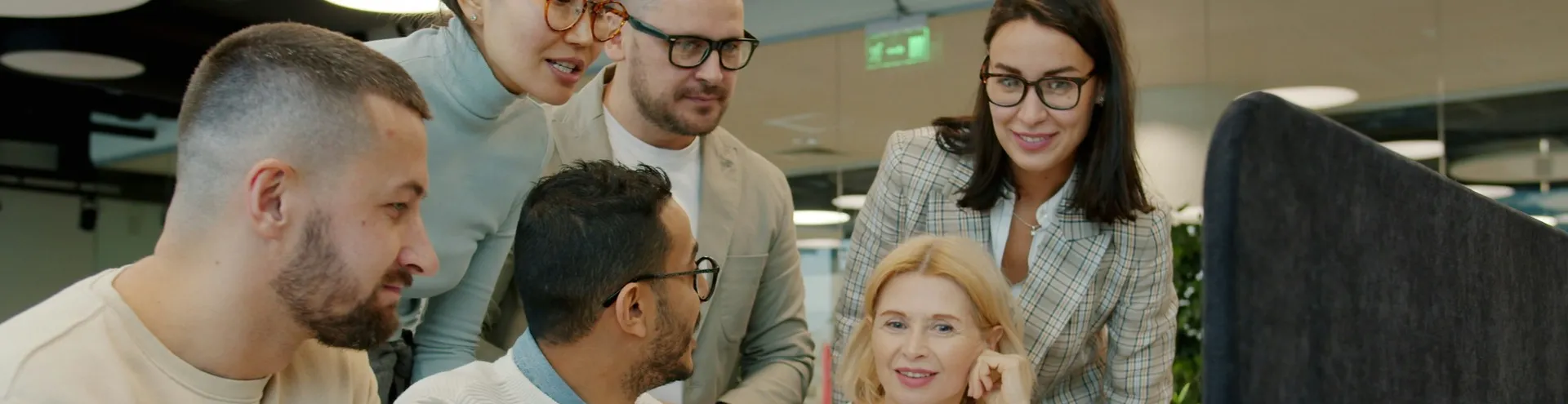 Equipe de profissionais reunida em volta de um notebook, colaborando em um ambiente de escritório moderno.