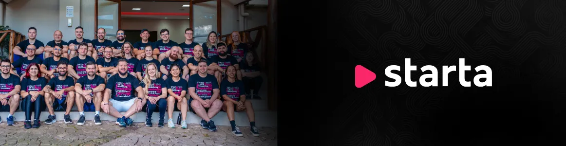 A imagem é dividida em duas partes:

Parte esquerda: um grupo grande de pessoas posa para uma foto em frente a um prédio. São cerca de 30 colaboradores, organizados em três fileiras (em pé, agachados e sentados). Todos vestem camisetas pretas com estampa colorida e sorriem para a câmera, transmitindo união e espírito de equipe.

Parte direita: fundo preto com textura de linhas curvas discretas. No centro está o logotipo da empresa Starta, com o nome em letras brancas minúsculas e um ícone em forma de triângulo rosa (lembrando o botão de “play”) à esquerda do texto.

Em resumo, a imagem mostra a equipe da Starta reunida e o logotipo da empresa lado a lado, reforçando identidade visual e espírito coletivo.