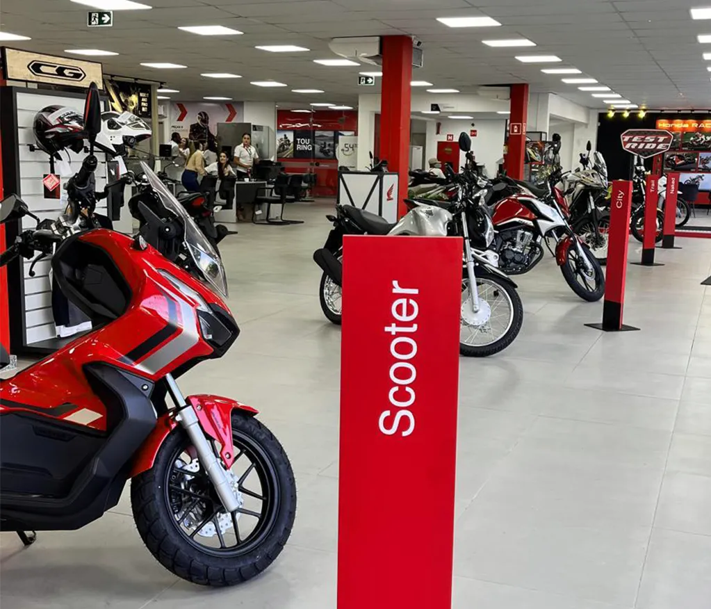 Showroom da concessionária com motocicletas alinhadas em categorias junto a expositores de acessórios Honda.