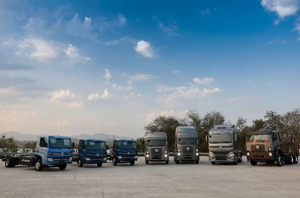 Linha de caminhões Volkswagen estacionados lado a lado em uma área aberta, sob um céu azul com nuvens claras. A imagem mostra diferentes modelos da marca, representando tecnologia, força e diversidade de produtos apoiados pela TRATON Financial Services Brasil.