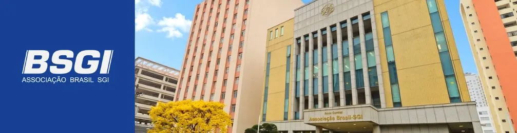 Banner institucional da BSGI (Associação Brasil SGI). À esquerda, fundo azul com o logotipo branco da BSGI e o texto ‘Associação Brasil SGI’. À direita, fotografia da fachada de um prédio moderno da associação, com detalhes em vidro e tons claros, localizado em área urbana cercada por edifícios altos. Em frente ao prédio, há uma árvore com flores amarelas sob céu azul com poucas nuvens.